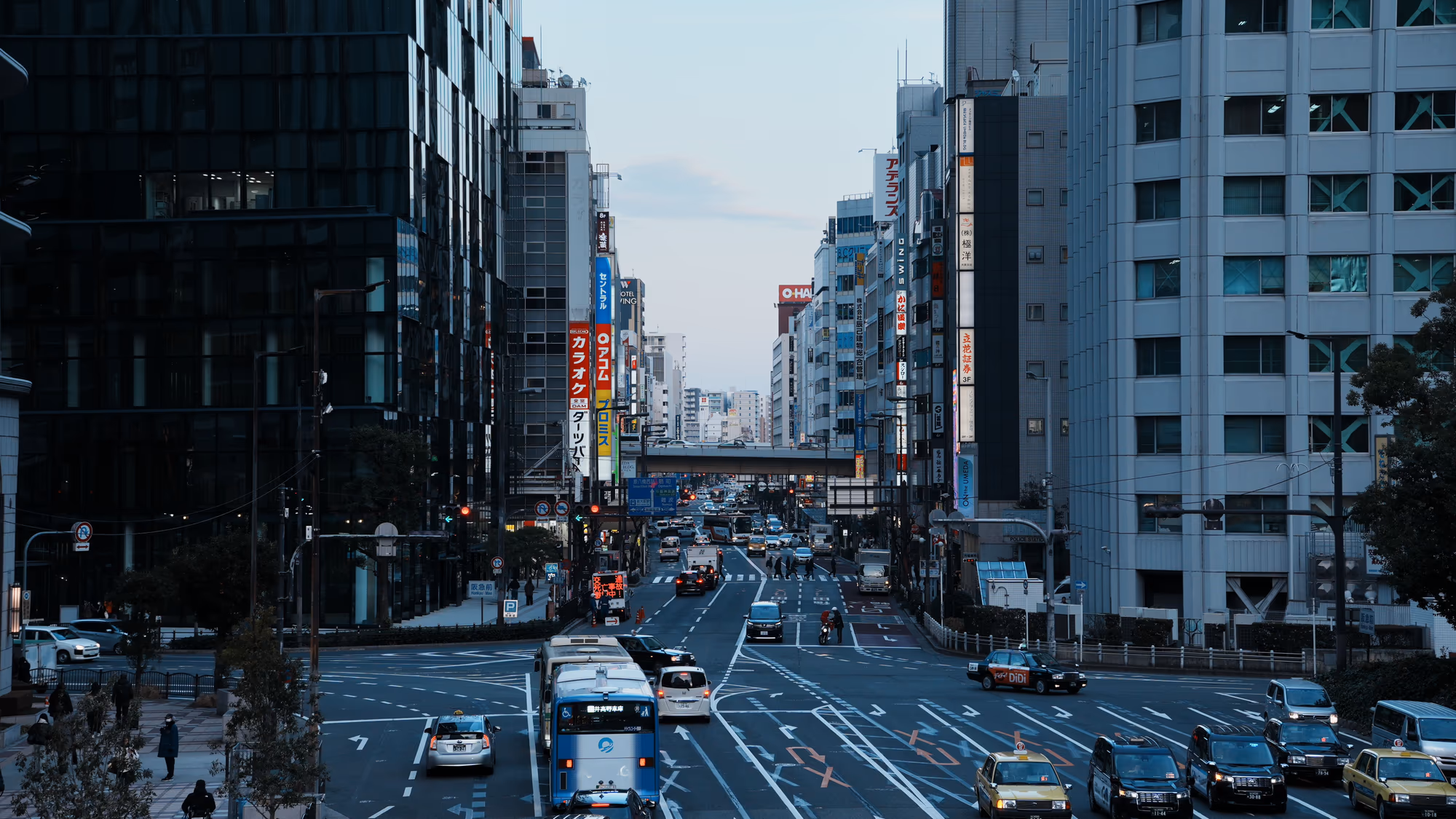 A broad Tokyo street with buses, taxis, buildings, and pedestrians